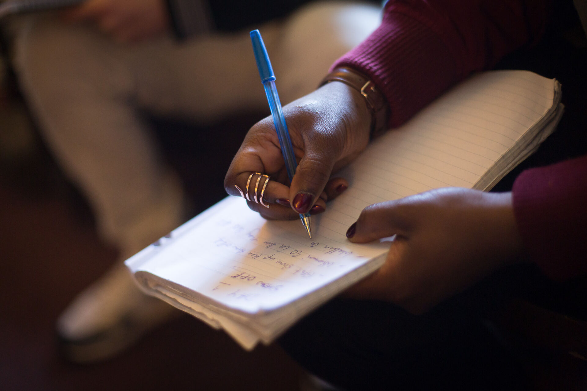 Image shows woman's hands wearing rings writing with a pen on a notepad