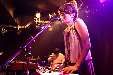 Young woman singing and playing a keyboard, inside club live music performance.