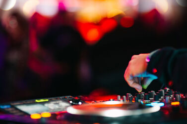Close up of a DJ's hand on a mixing desk. Blurry shadows of club goers in the background.