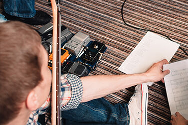 Young person holding a guitar sitting on the floor sharing a sheet of music.