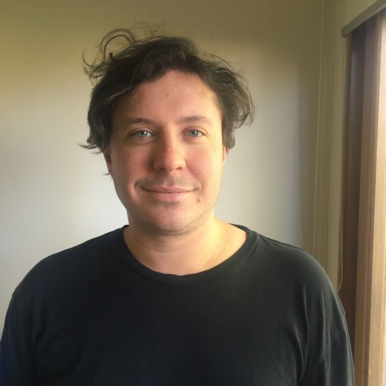 Oscar is looking at the camera, smiling. He has brown hair and is wearing a black tshirt.