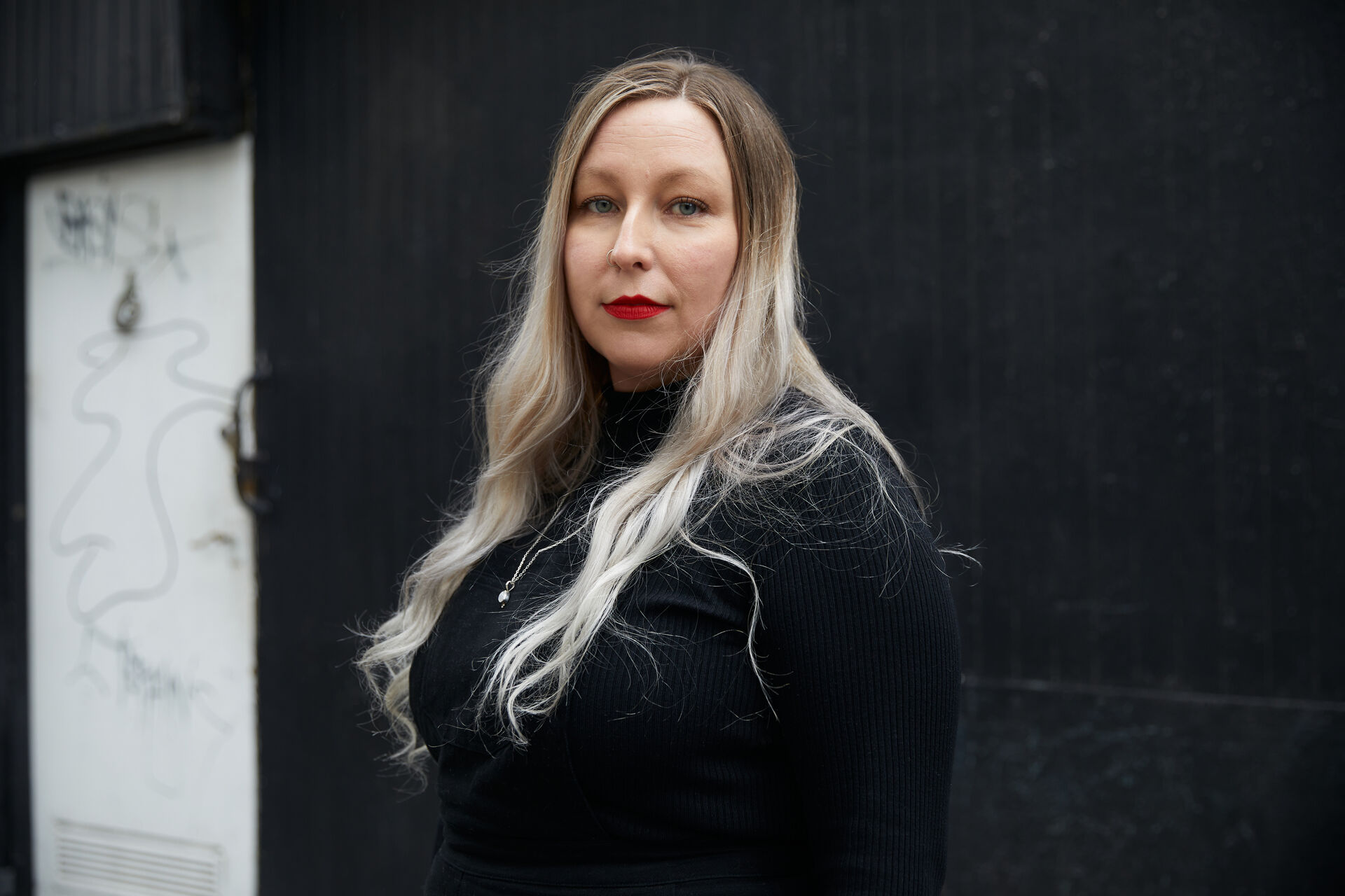 Katarzyna is standing side on, looking at the camera. She has long blonde hair and is wearing red lipstick and a black top.