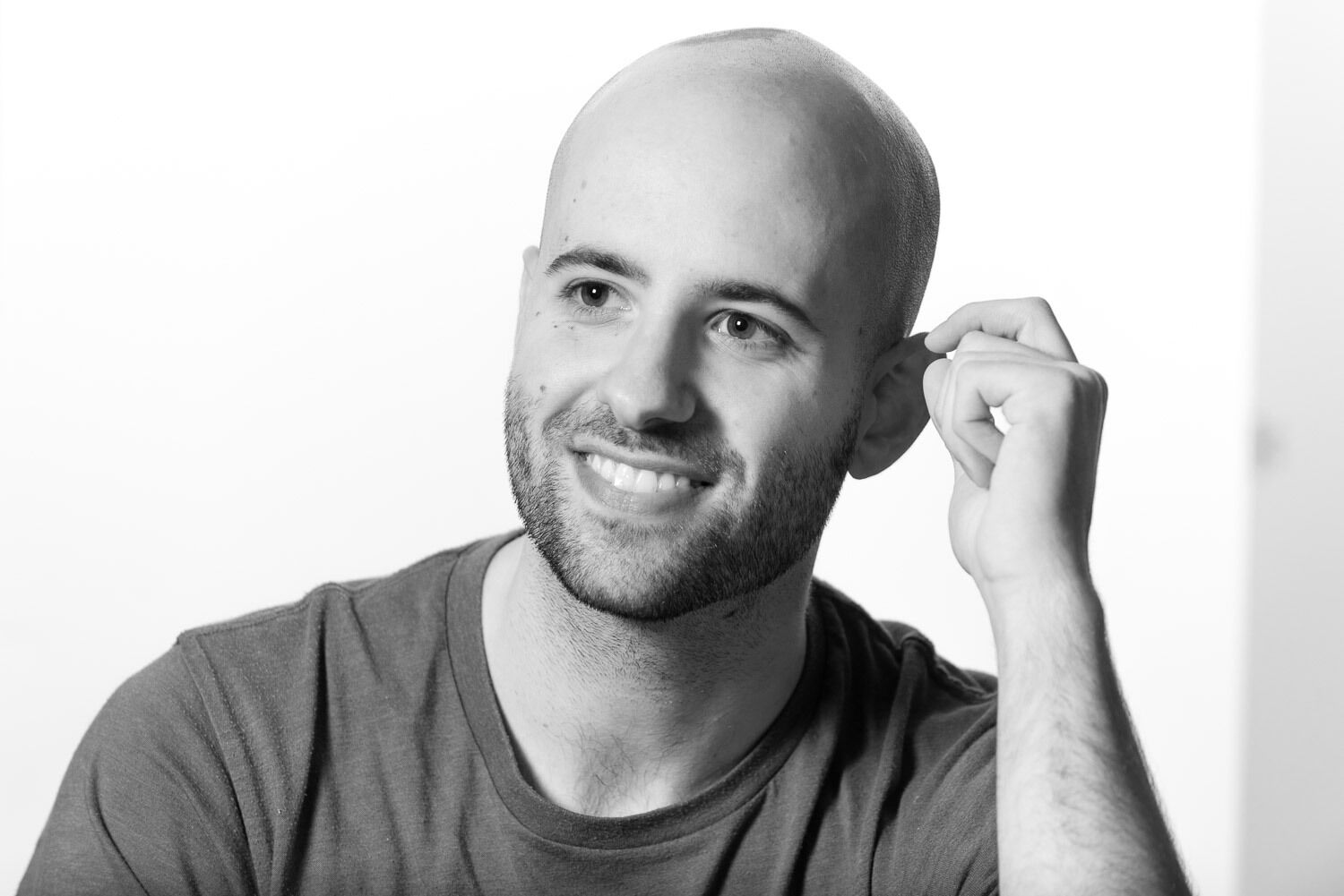 Black & white photo of Simon looking past the camera. His arm is up and he is smiling.