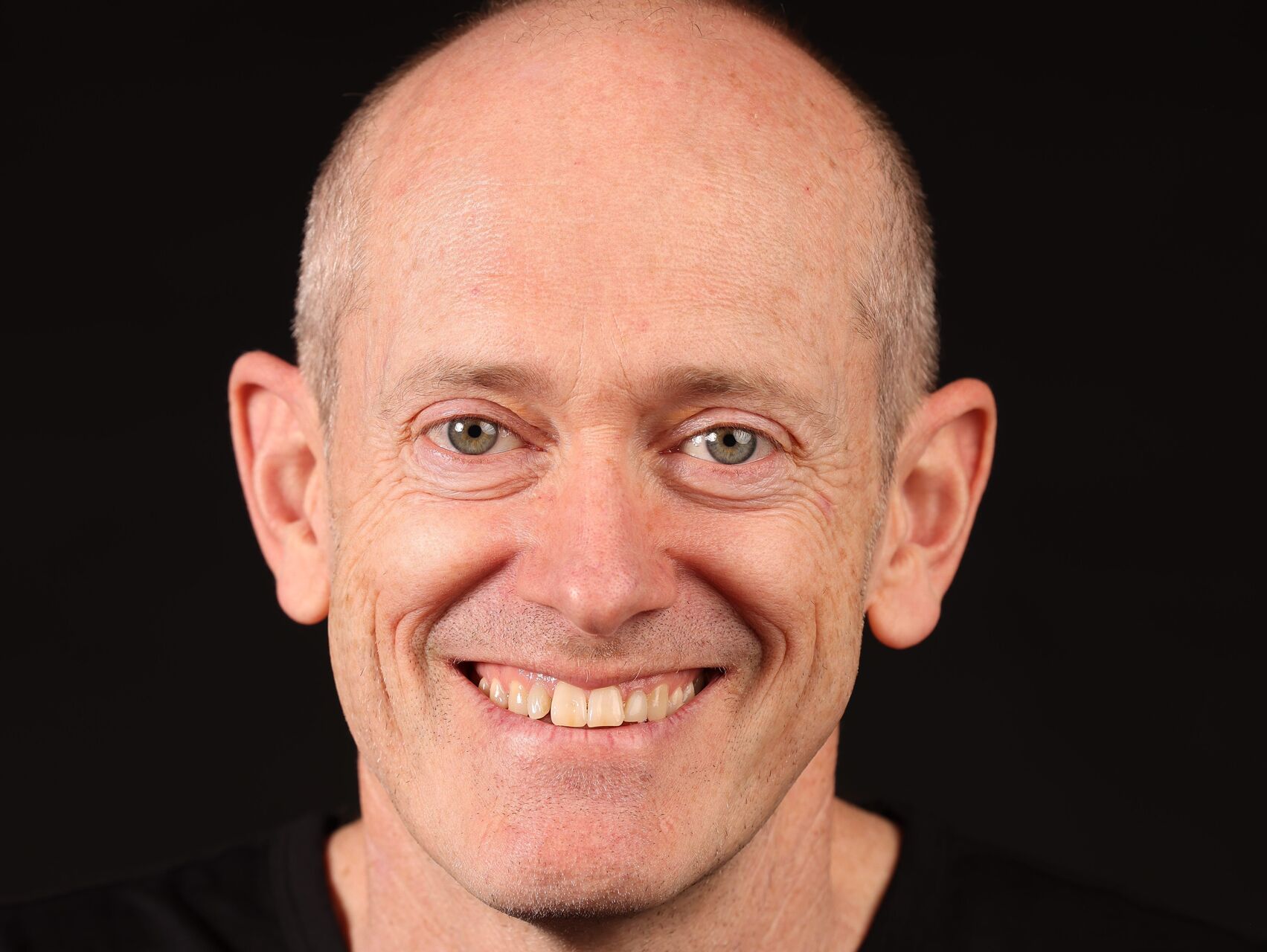 Head shot of Yon Hall on a black background. He is wearing a black tshirt and is looking at the camera, smiling.