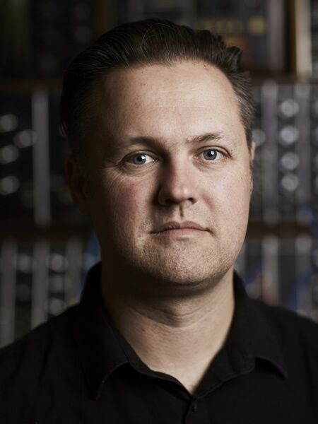 Byron is looking directly to the camera and is wearing a black polo shirt.