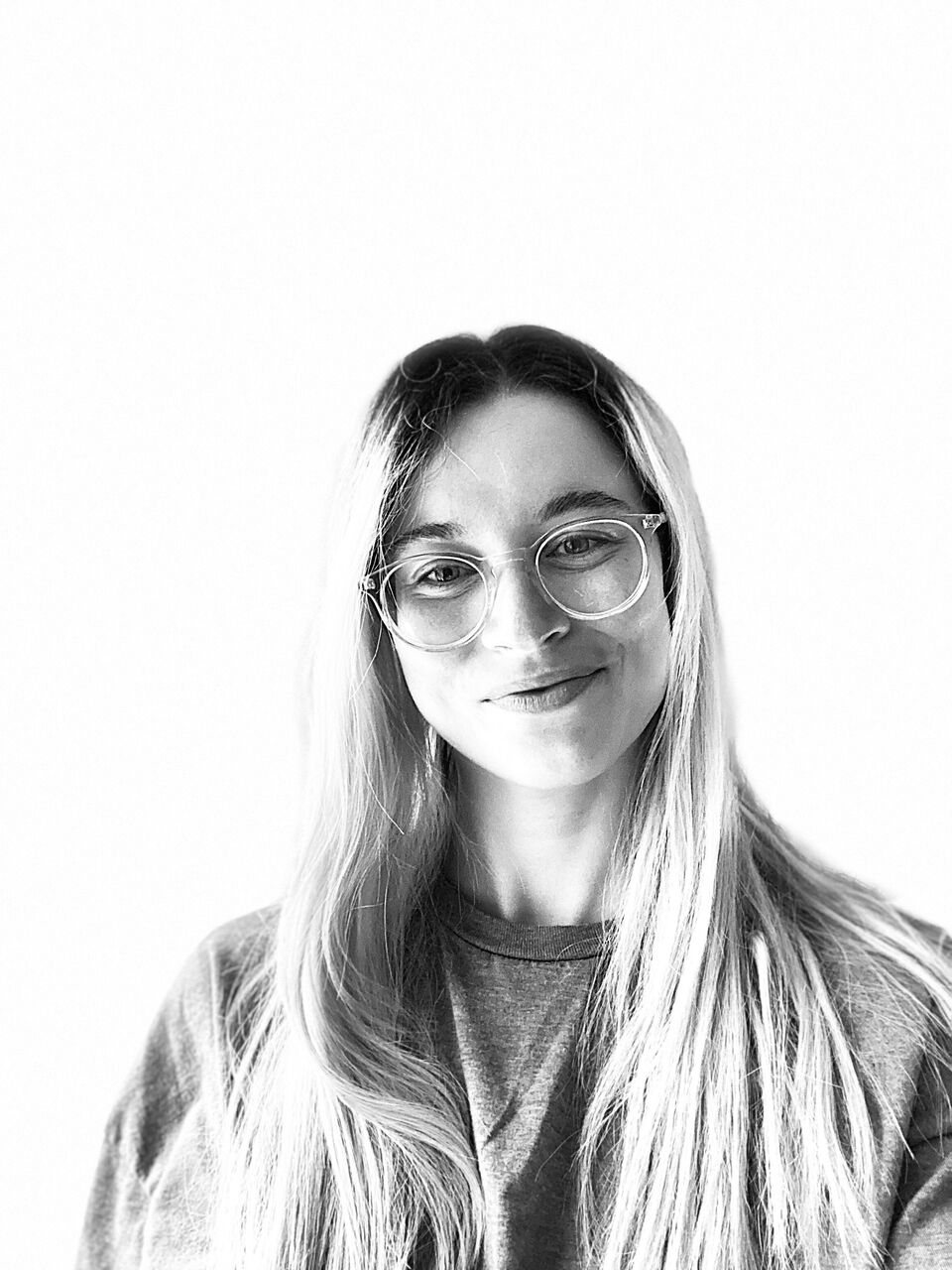 This is a black & white photograph of Samantha. She has long light coloured hair, is wearing glasses and is looking at the camera, smiling. She is wearing a tshirt.