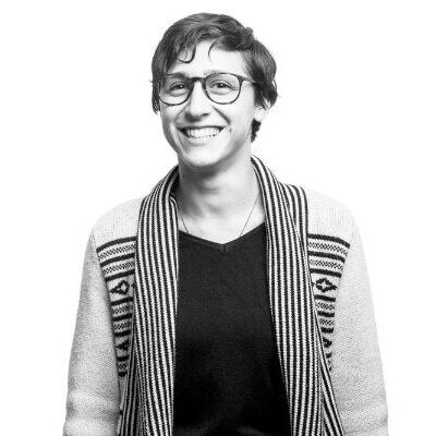 Black & white photo of talia. They are wearing glasses, looking at the camera, smiling.