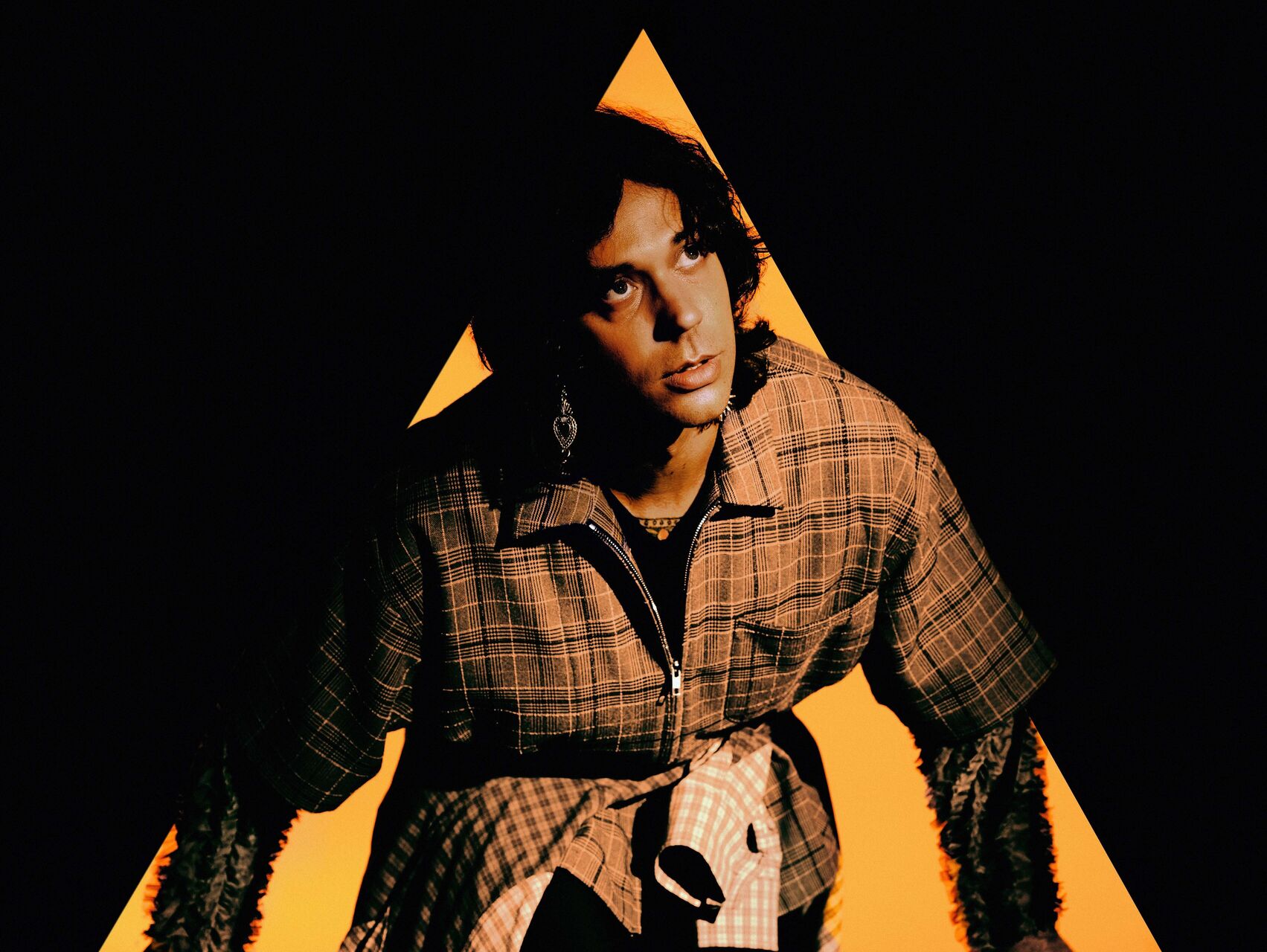 Zeppelin is photographed so that it looks like he is coming out of a yellow triangle. He is wearing a brown jacket and has dark hair. He is looking upwards and away from the camera.