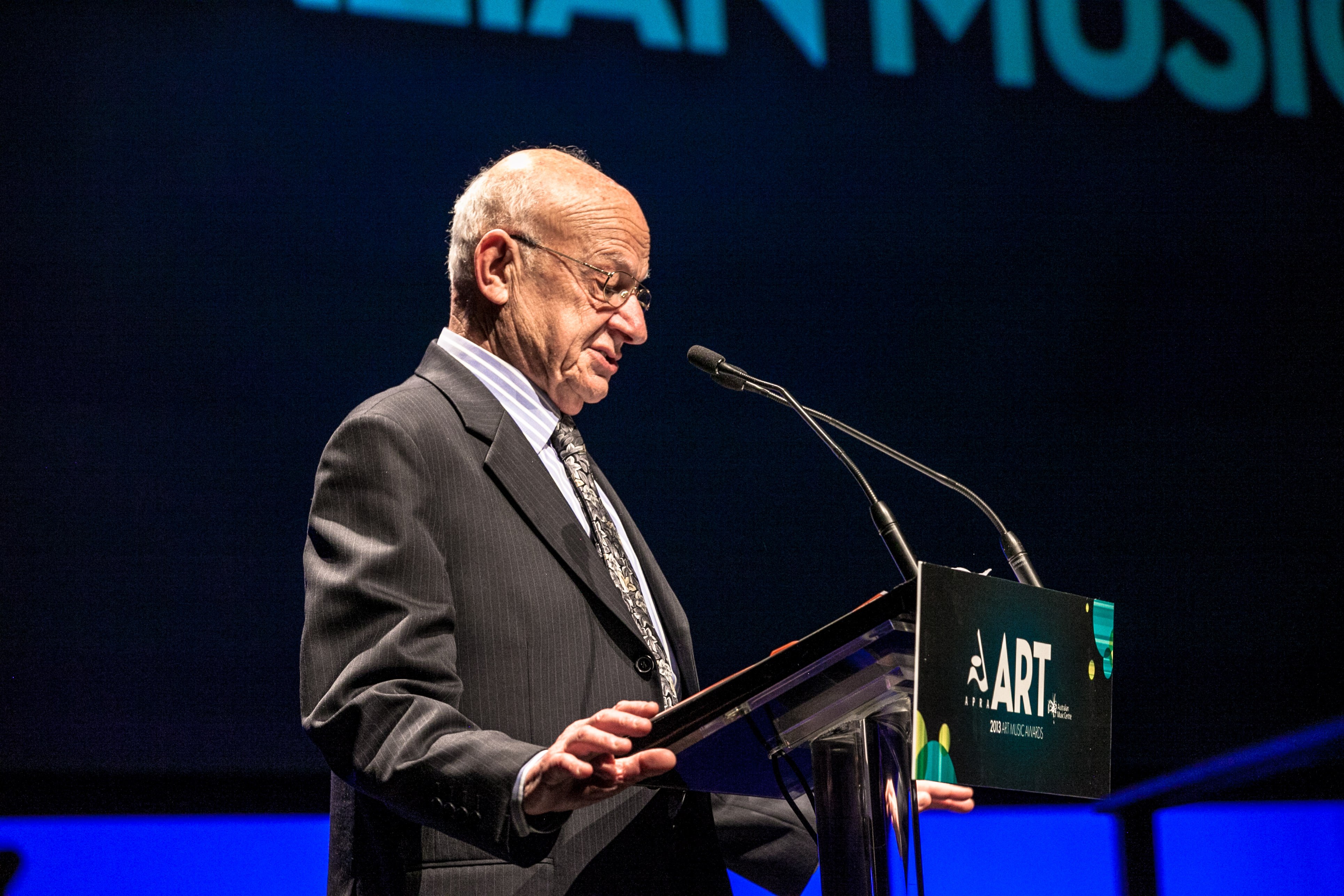 George Dreyfus wearing a suit standing at a lectern on stage