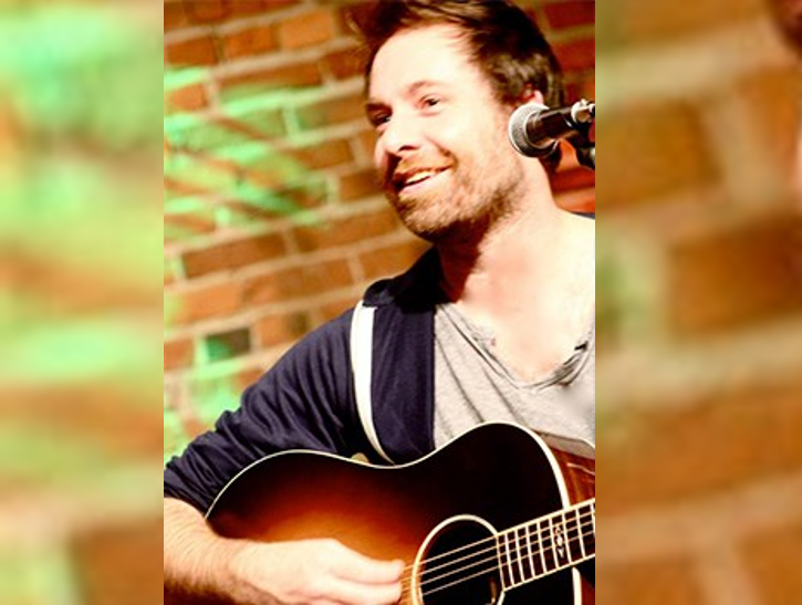Songwriter Phil Barton plays guitar in front of a brick wall