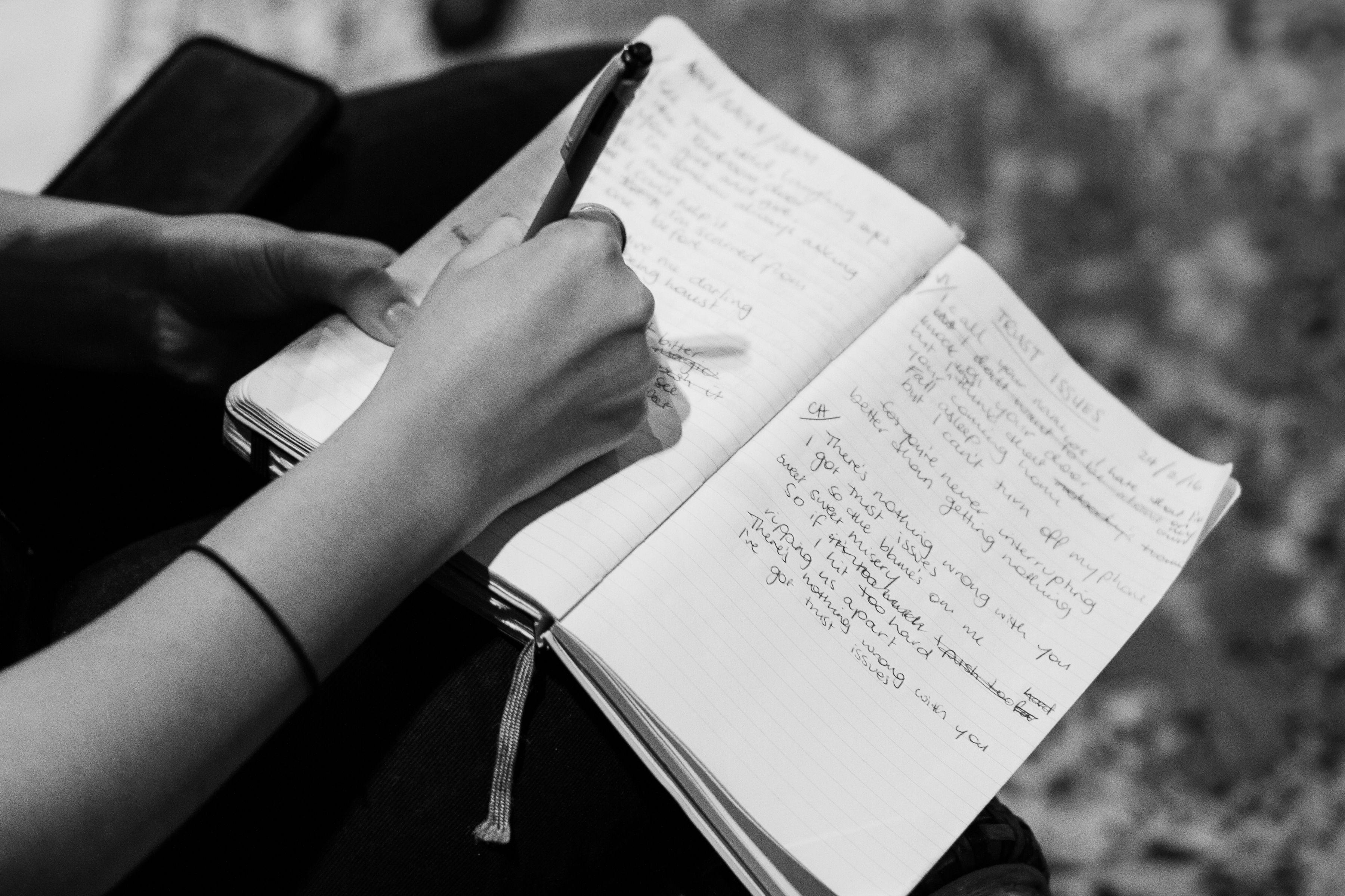 A black and white image of a hand writing lyrics