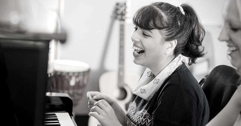Young girl laughing as she sits in front of a piano